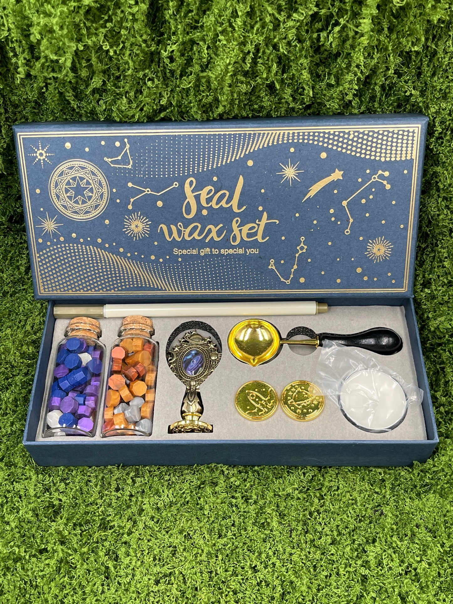 A seal wax set displayed on a green surface, including a variety of items such as wax sticks, a melting spoon, a seal stamp, a tea light candle, and additional stamp heads.