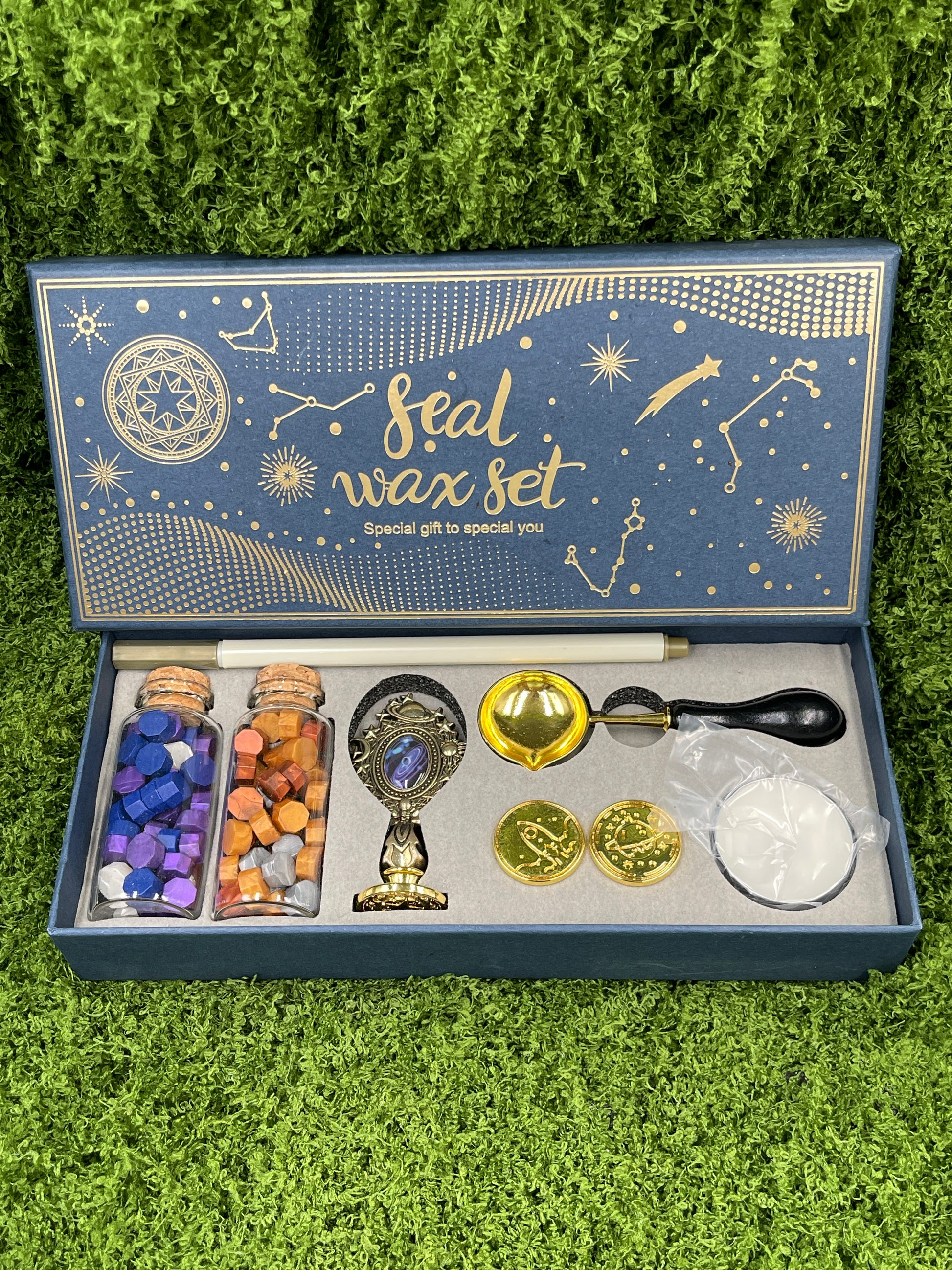 A seal wax set displayed on a green surface, including a variety of items such as wax sticks, a melting spoon, a seal stamp, a tea light candle, and additional stamp heads.