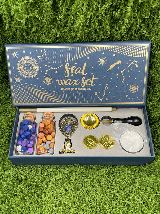 A seal wax set displayed on a green surface, including a variety of items such as wax sticks, a melting spoon, a seal stamp, a tea light candle, and additional stamp heads.
