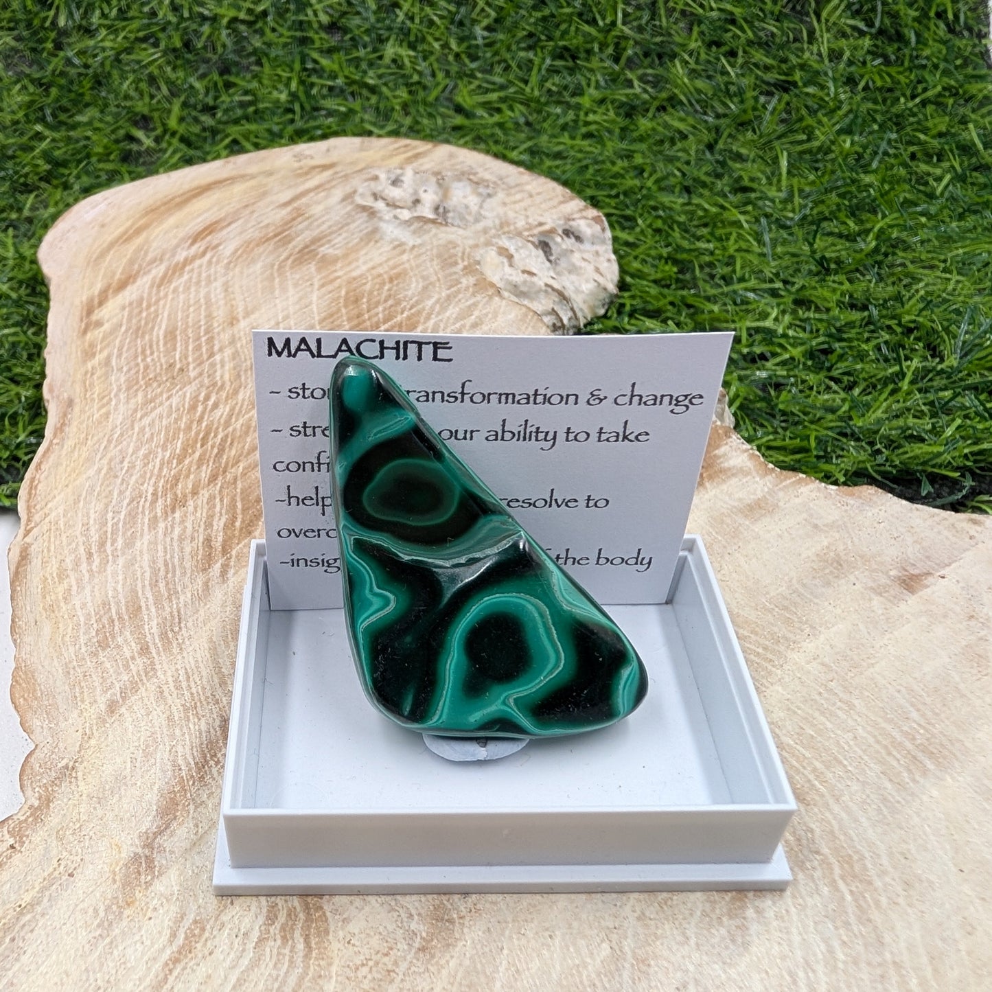 Malachite stone in a box with a card on a grassy background