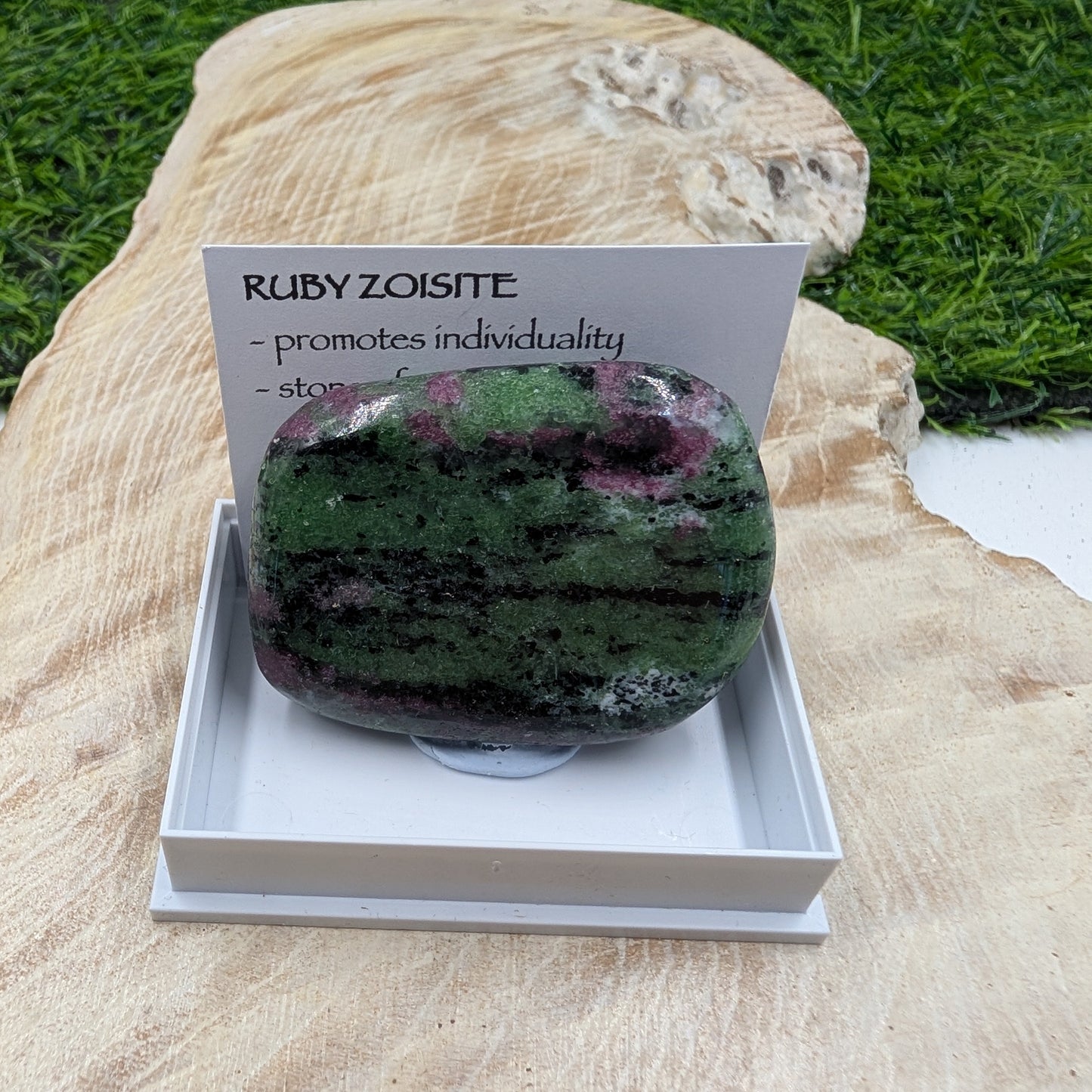Ruby zoisite stone with descriptive card on a wooden surface
