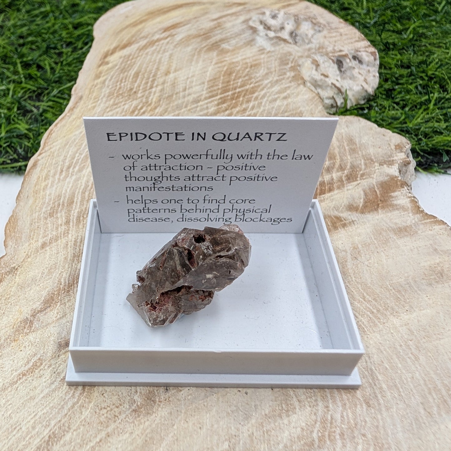 Mineral sample in a display box with descriptive card on a natural stone background