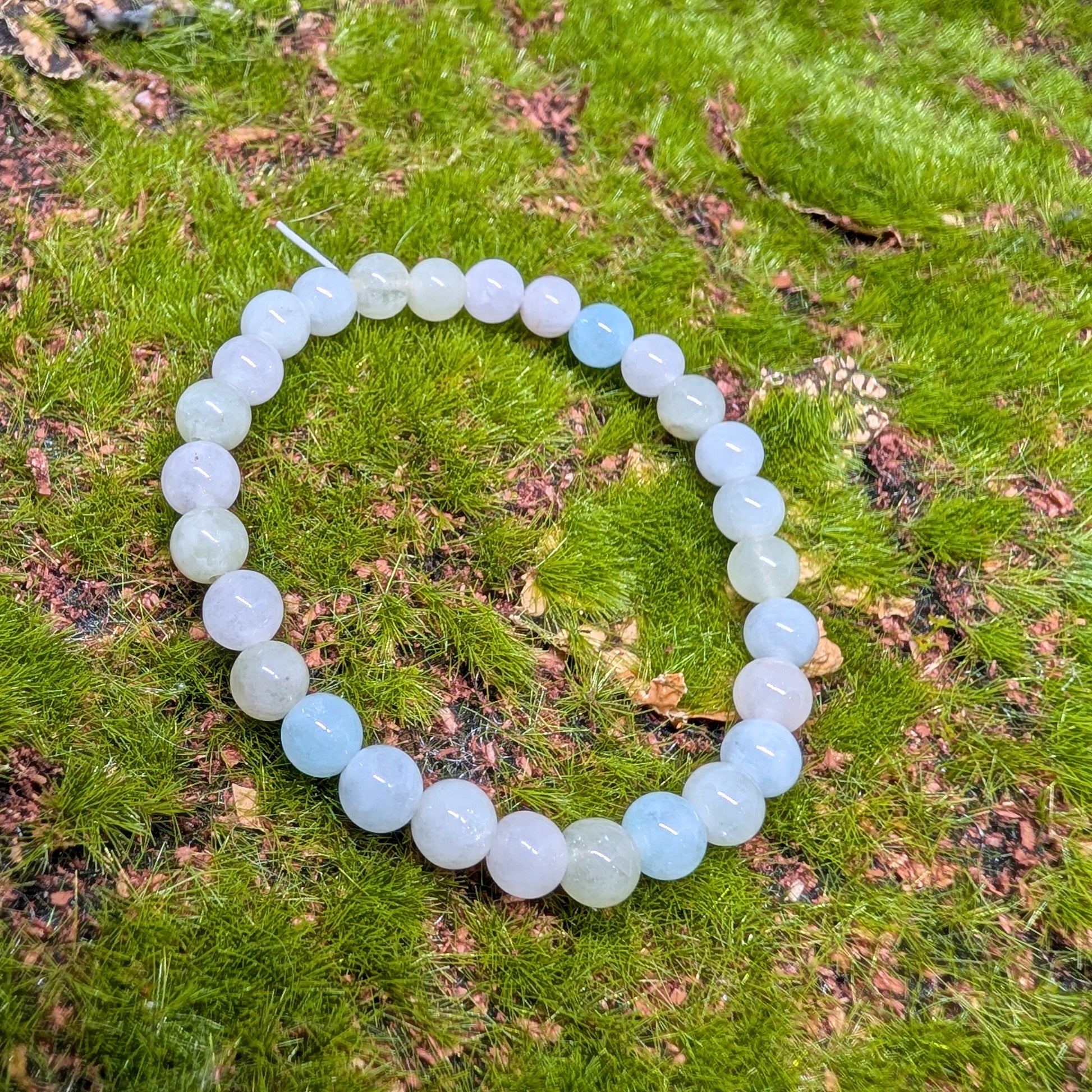 White beaded bracelet on a green mossy surface