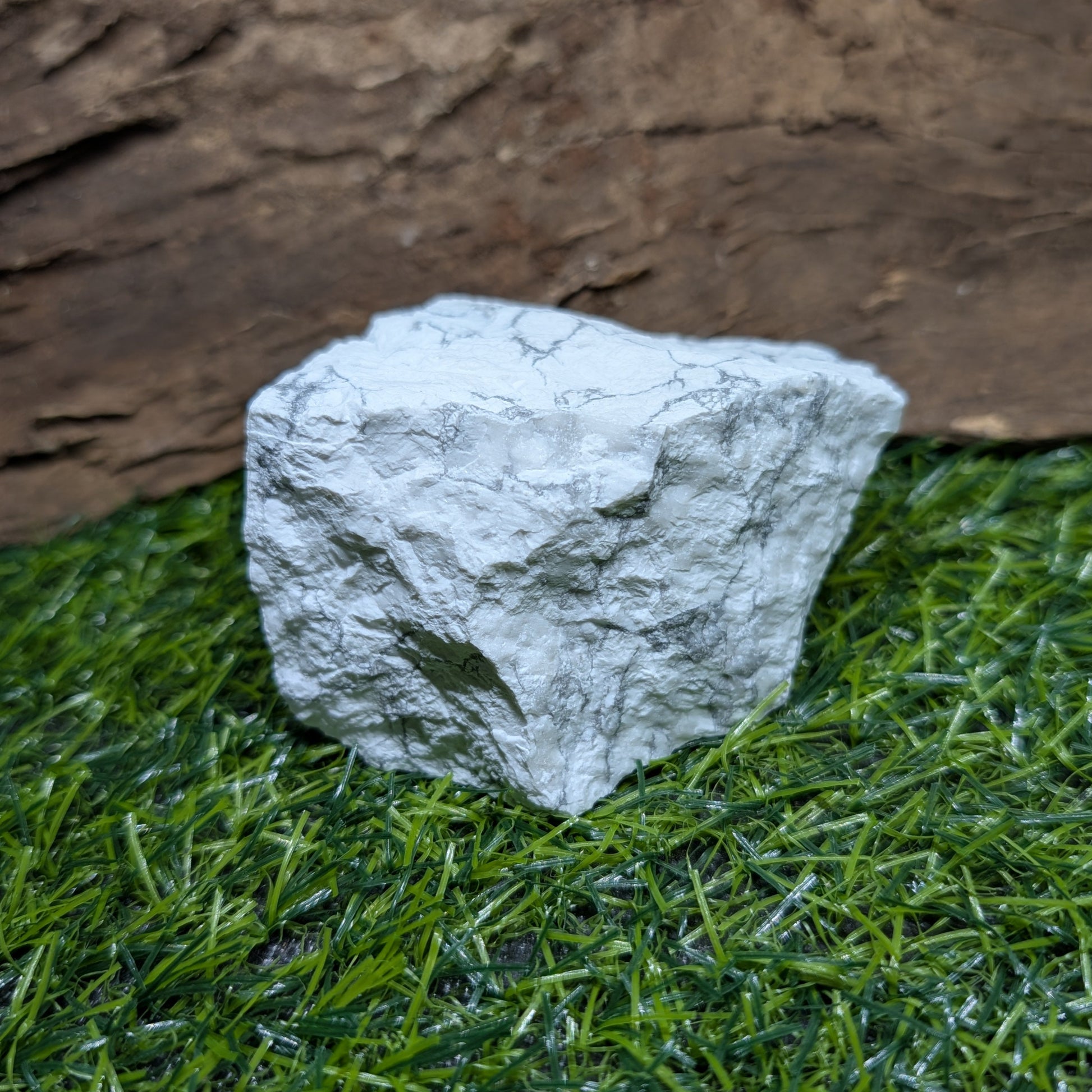 White stone on artificial grass with a wooden log in the background