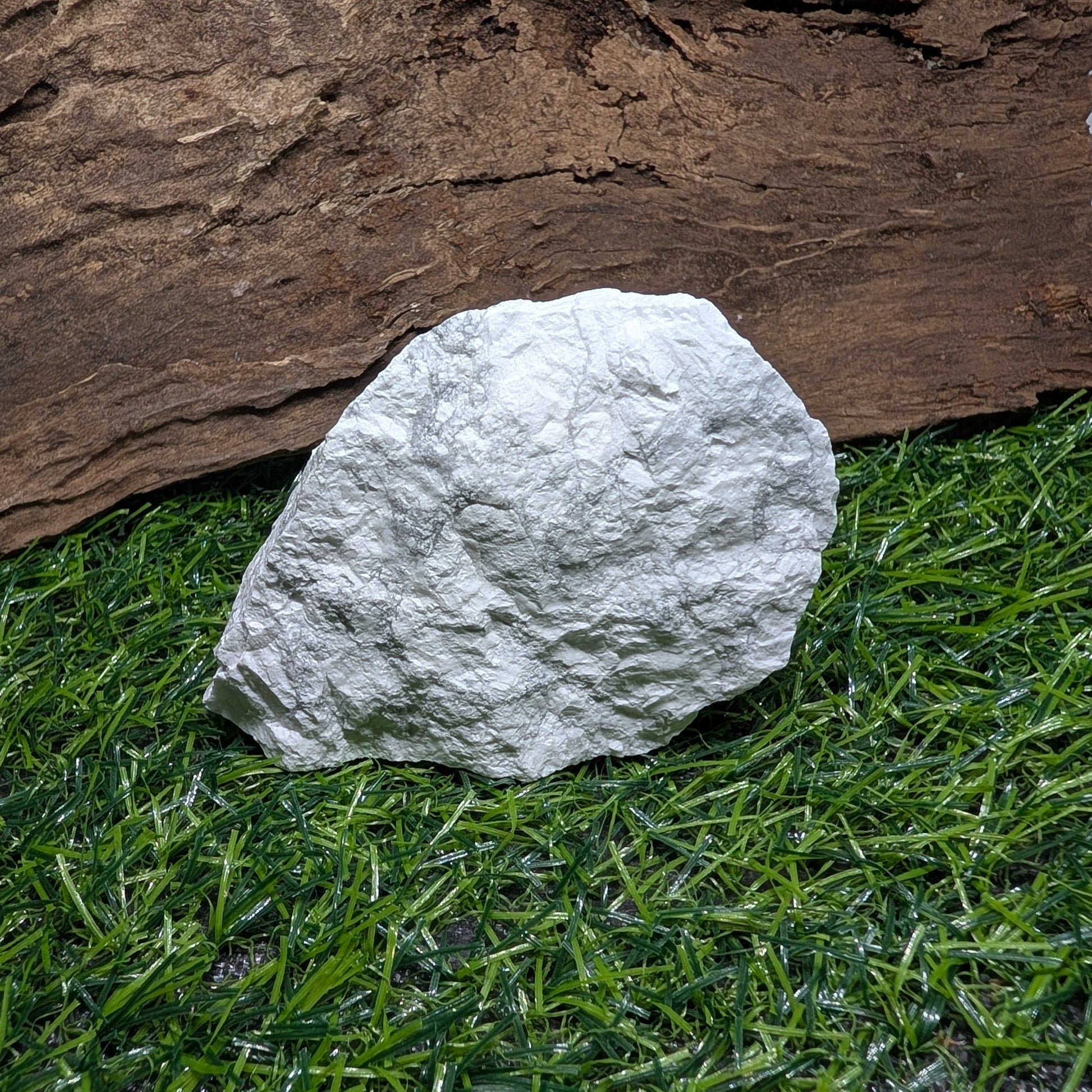 White stone on artificial grass with a wooden log in the background