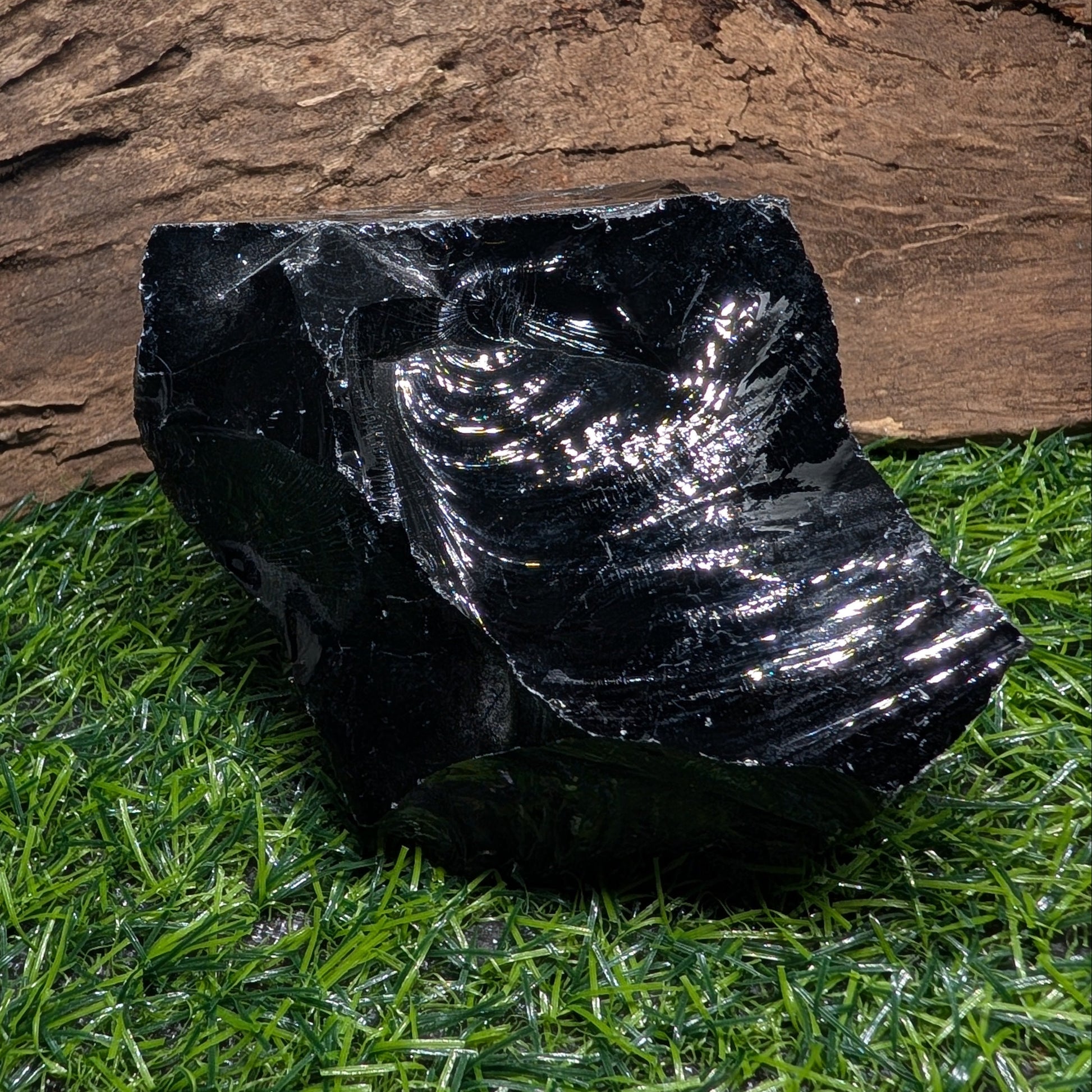 Black rubber boot on artificial grass with a wooden log in the background