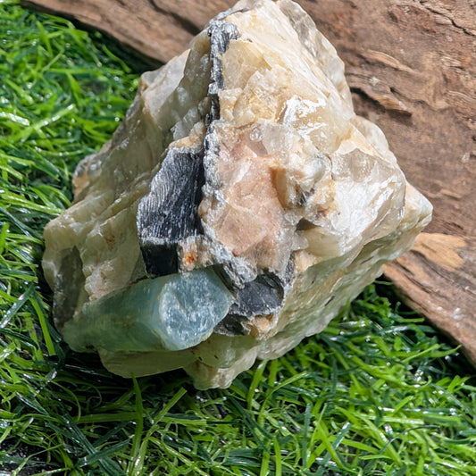 Mineral specimen on grass with a wooden log in the background