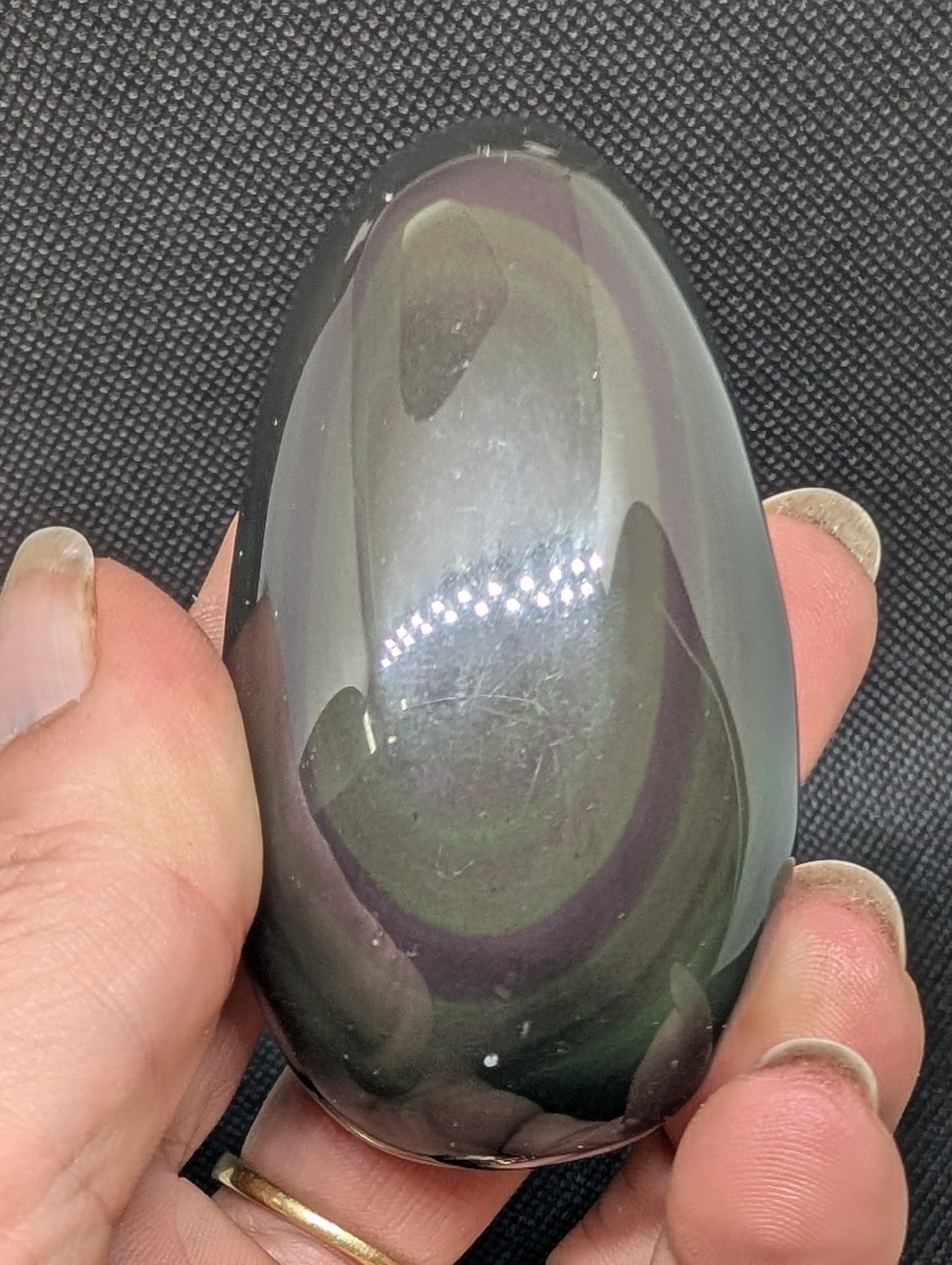 Hand holding a reflective oval object against a dark background