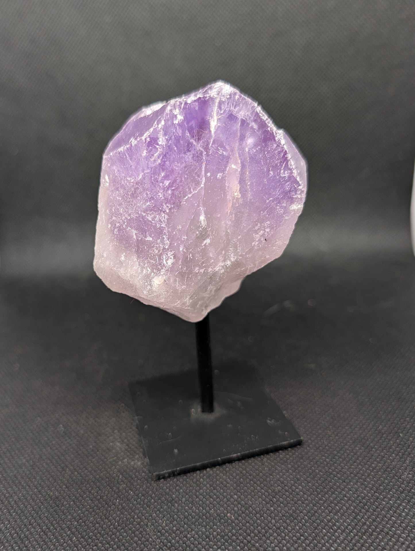 Amethyst crystal on a black stand against a dark background