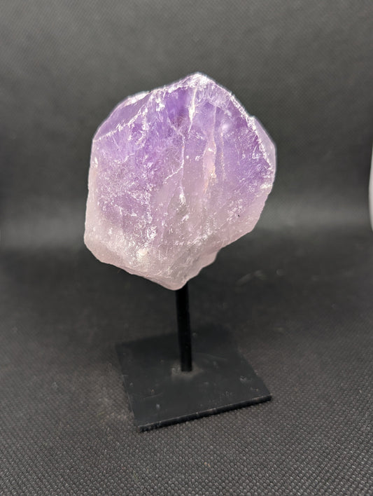 Amethyst crystal on a black stand against a dark background