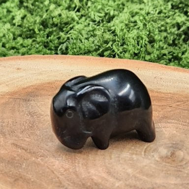 Black elephant figurine on a wooden surface with green grass in the background