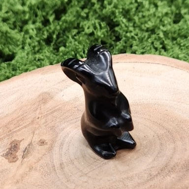 Black stone sculpture of a bear on a wooden surface with green grass in the background