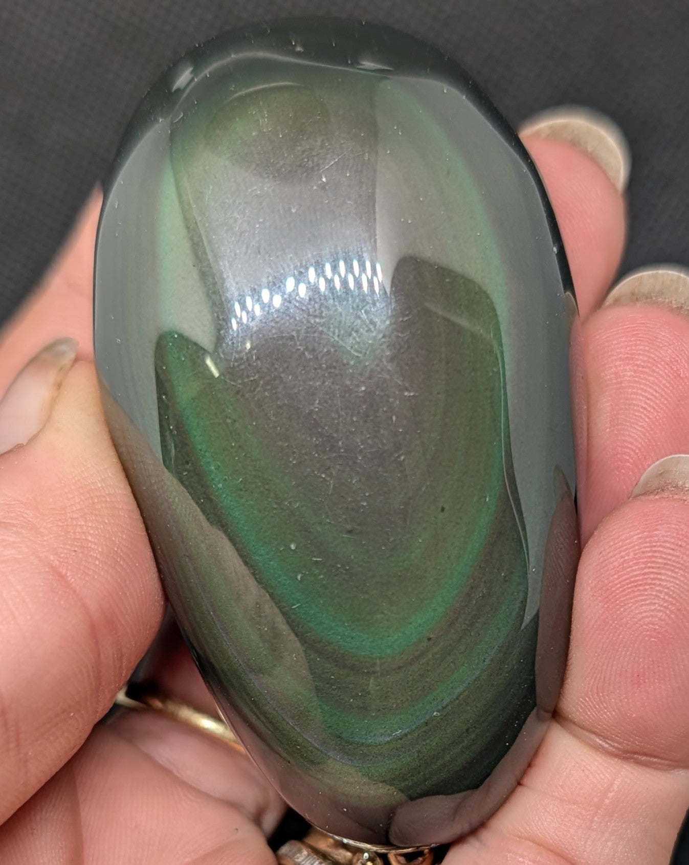 Hand holding a polished green stone with a dark background
