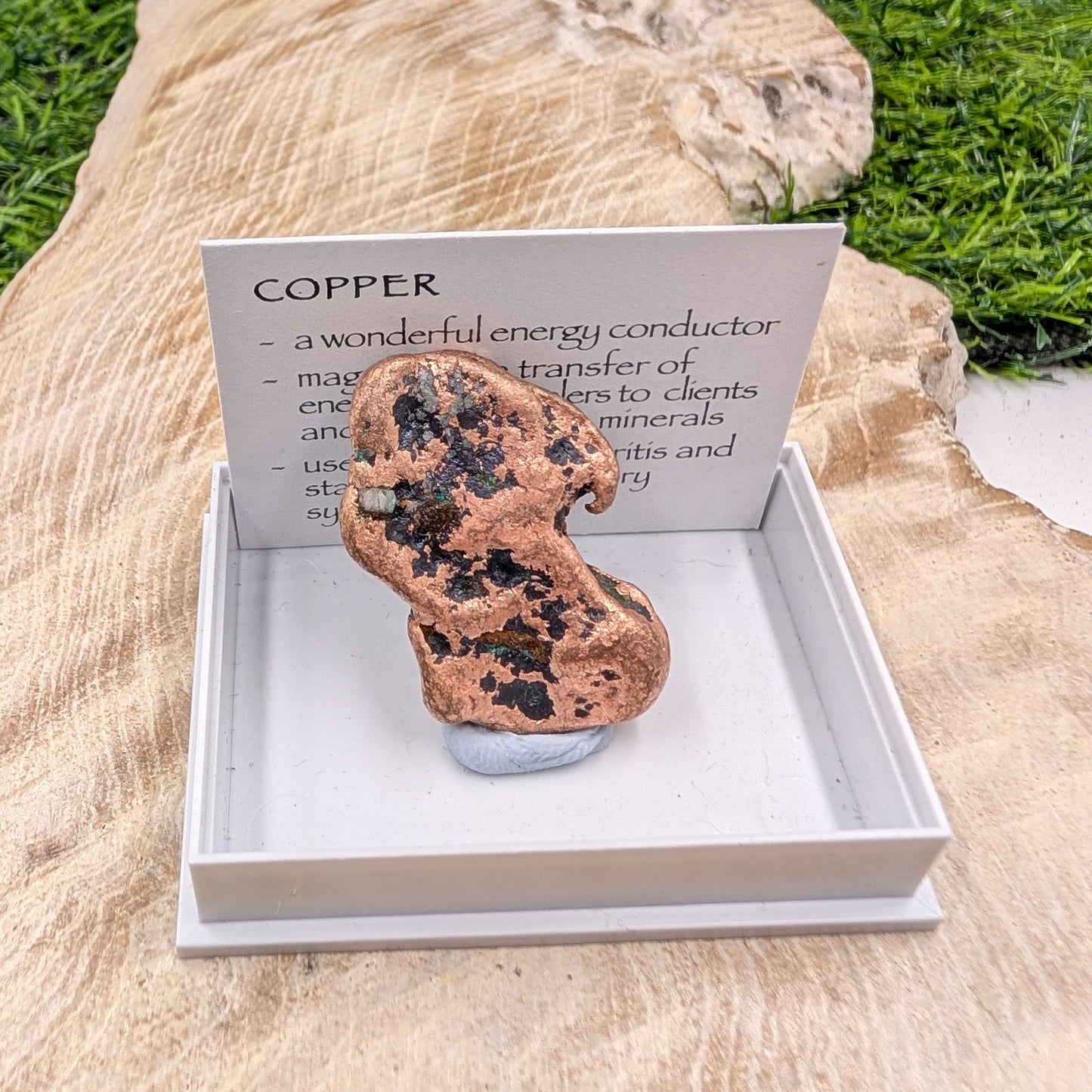 Copper mineral specimen in a display box with an informational card on a natural stone background.