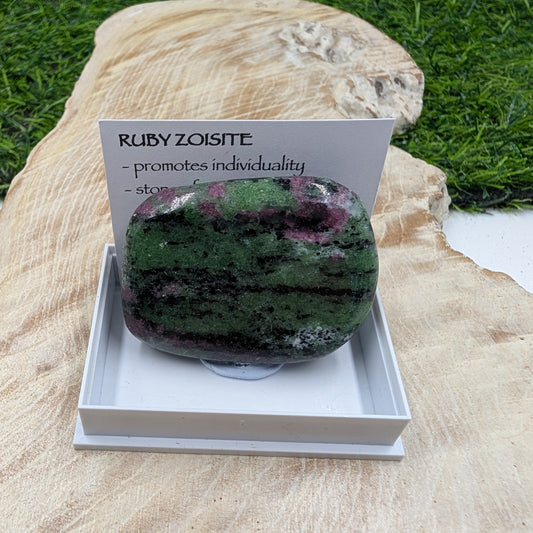 Ruby zoisite stone with descriptive card on a wooden surface