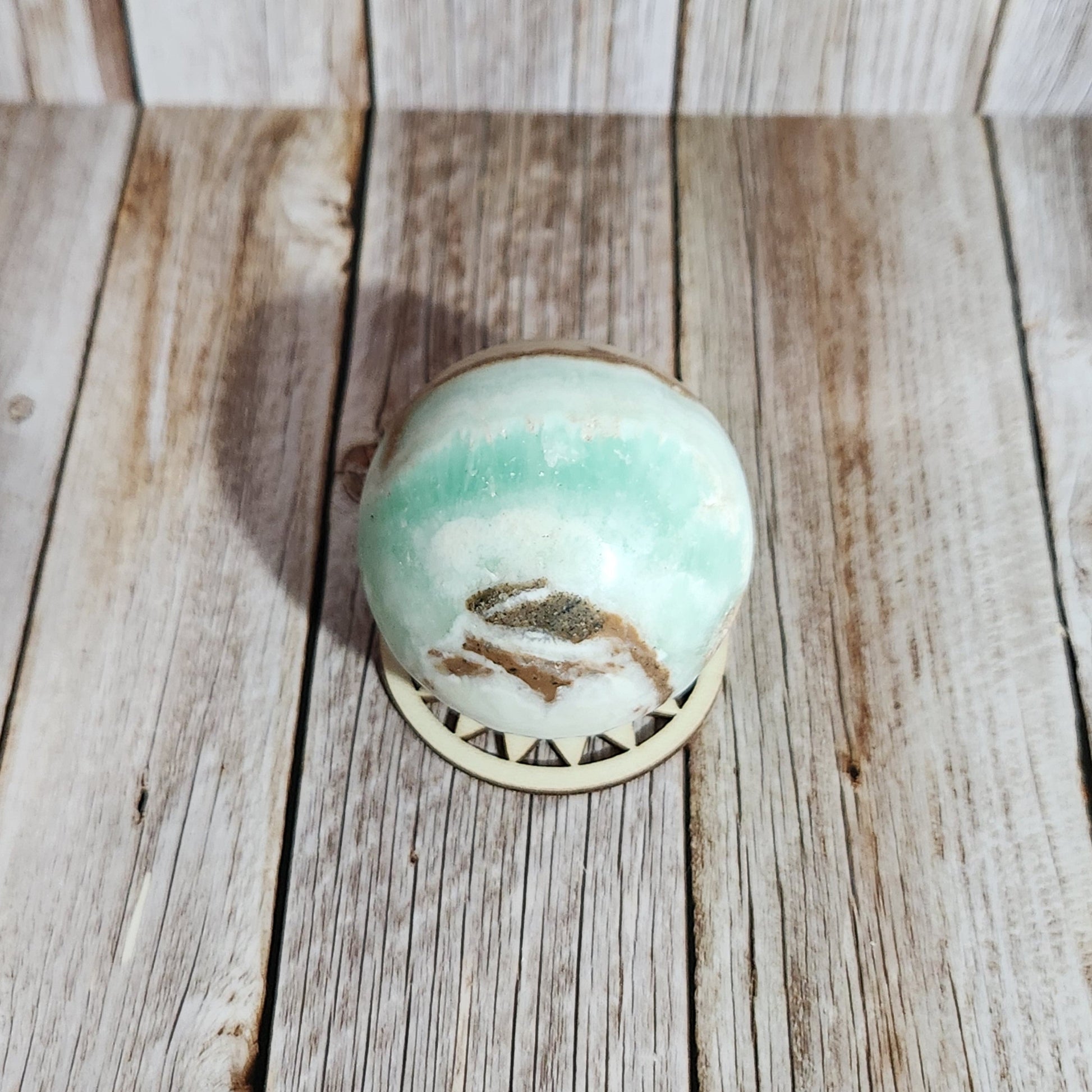 Round ceramic knob with a green glaze and gold leaf design on a wooden surface