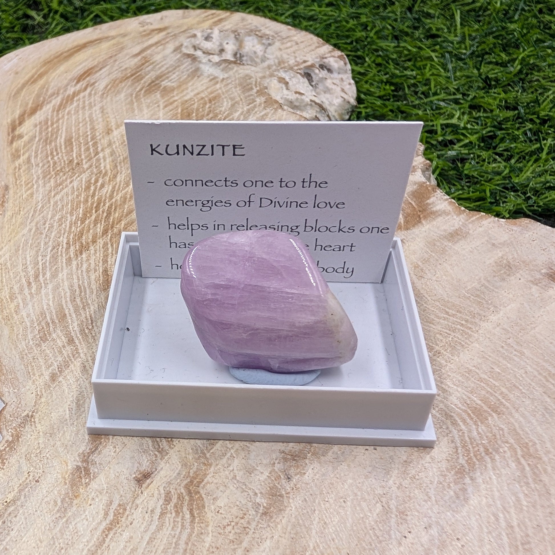 Purple kunzite crystal in a box with descriptive card on a wooden surface