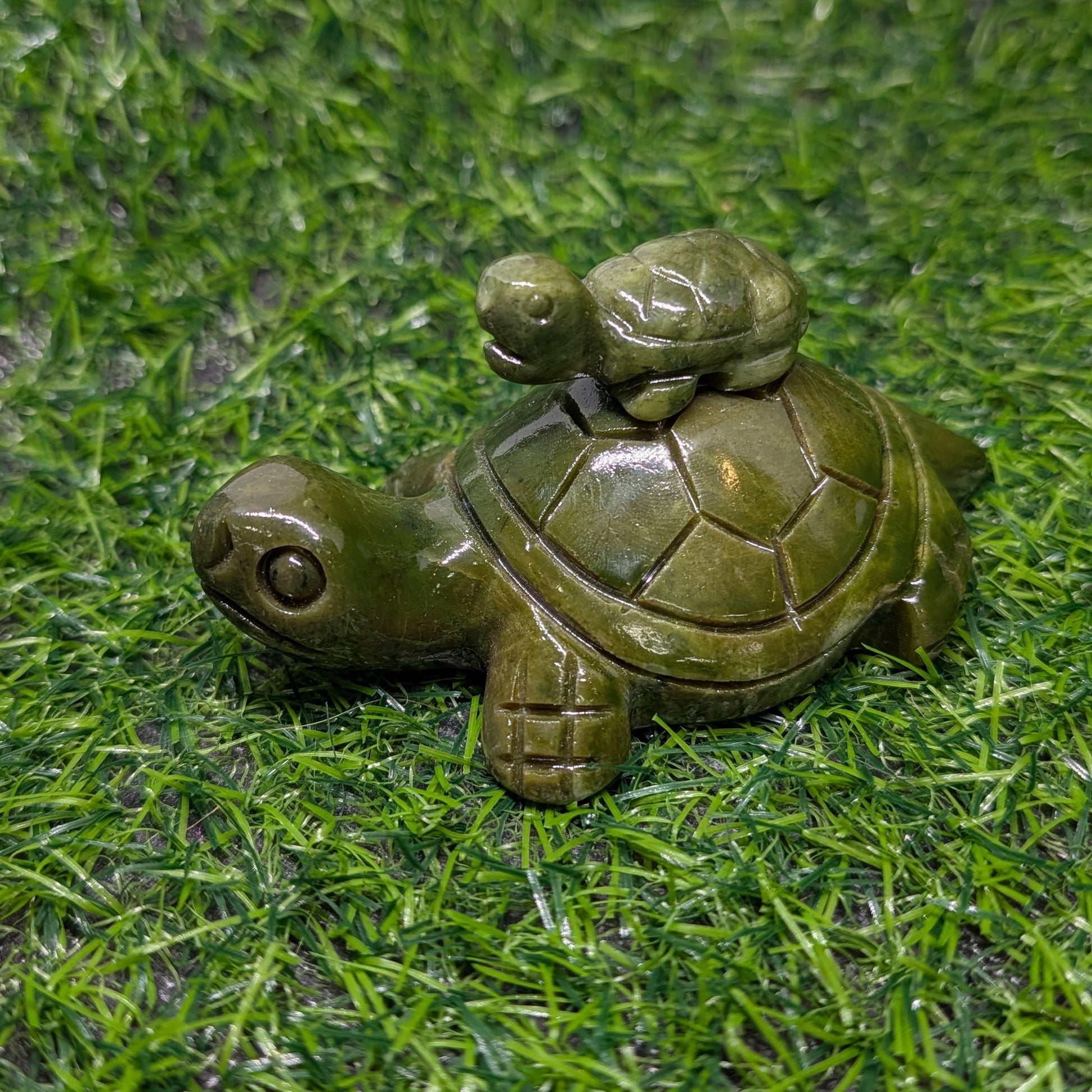 Decorative turtle figurine with a smaller turtle on its back, placed on green grass.
